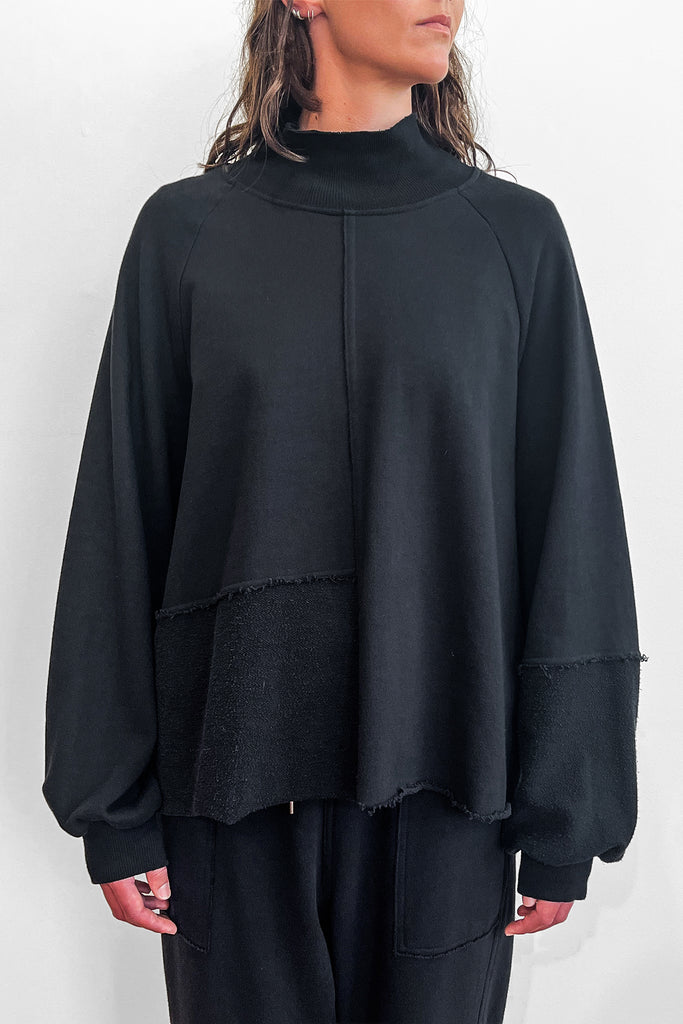 Close up of a model wearing an oversized black cotton sweater with track-pants