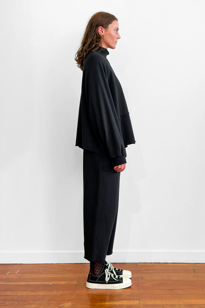Side view of a model wearing an oversized black cotton sweater with track-pants