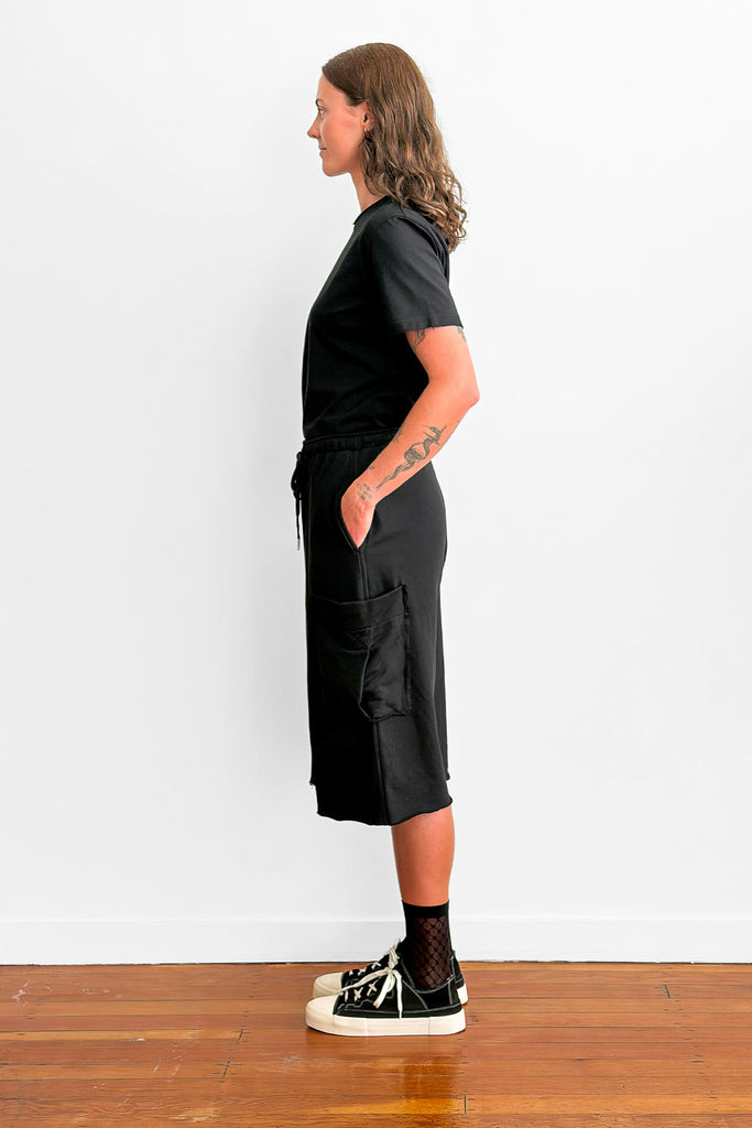 Side view of a model wearing a black t-shirt tucked into oversized, long black shorts