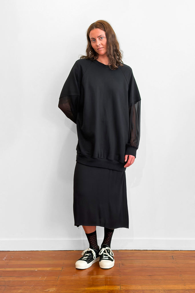 Model wearing an oversized black sweater with sheer silk sleeves. Worn over a black dress