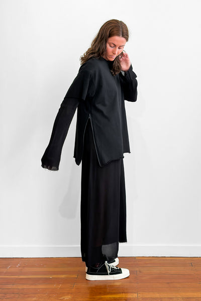 Side view of a model wearing an oversized black t-shirt over a long black dress. The t-shirt has a side zip detail