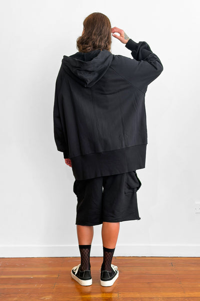 Back view of a model wearing an long, oversized black zip-up hoodie with shorts