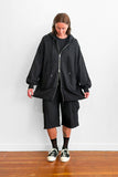 Model wearing an long, oversized black zip-up hoodie with shorts