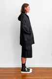 Side view of a model wearing an long, oversized black zip-up hoodie with shorts