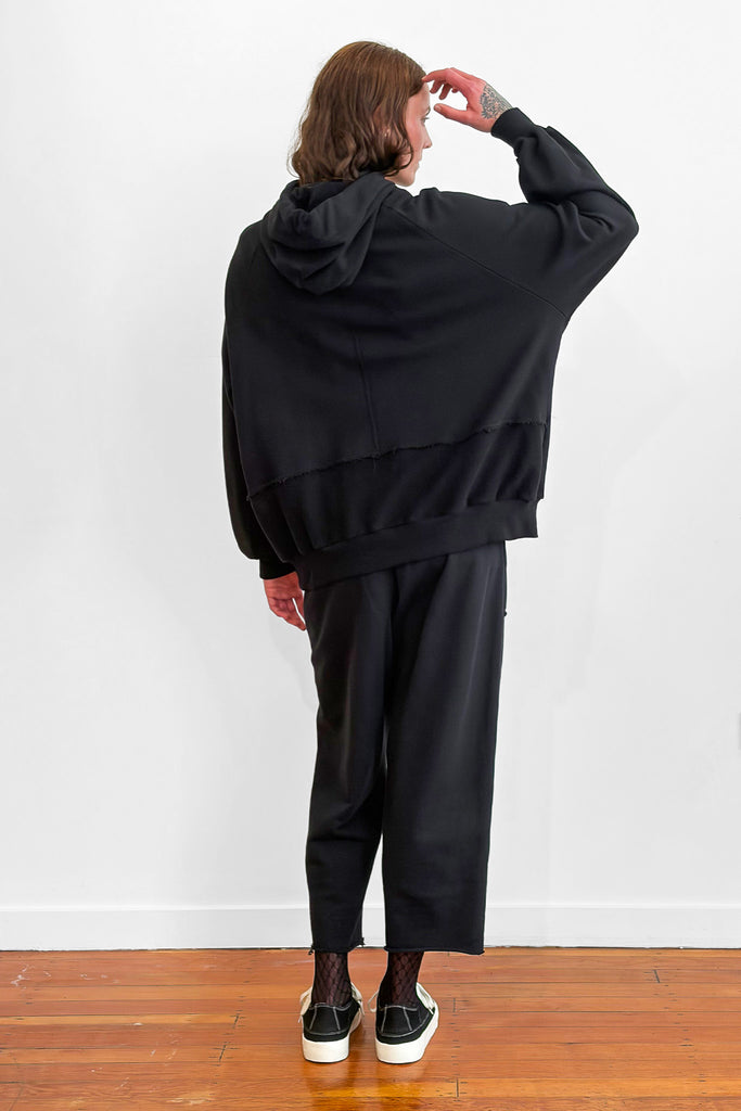 Back view of a model wearing an oversized black cotton hoodie with track-pants