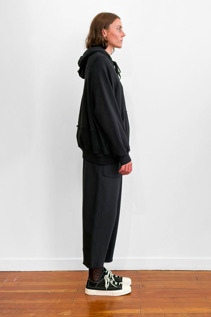 Side view of a model wearing an oversized black cotton hoodie with track-pants