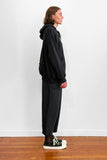 Side view of a model wearing an oversized black cotton hoodie with track-pants