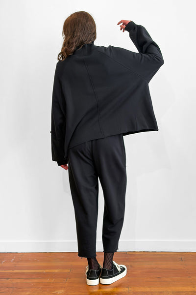 Back view of a model wearing an oversized black cotton sweater with track-pants