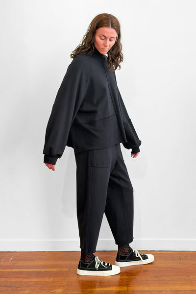 Side view of a model wearing an oversized black cotton sweater with track-pants