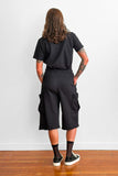 Back view of a model wearing a black t-shirt tucked into oversized, long black shorts