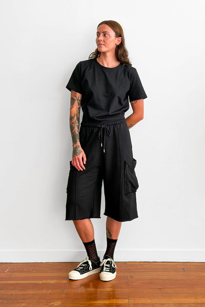 Model wearing a black t-shirt tucked into oversized, long black shorts