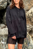 Model wearing an oversized black zip sweater over a mini black dress. Standing infront of a rocky wall