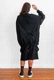Back view of a model wearing an oversized black sweater with sheer silk sleeves, and shorts
