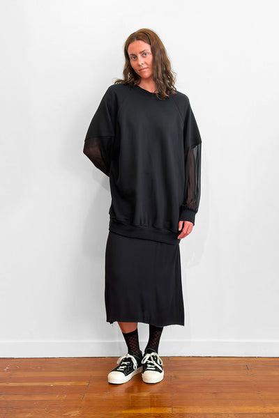 Model wearing an oversized black sweater with sheer silk sleeves. Worn over a black dress