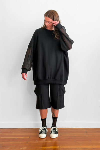 Model wearing an oversized black sweater with sheer silk sleeves, and shorts
