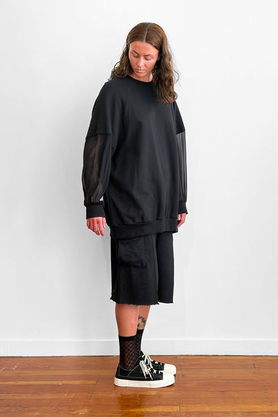Model wearing an oversized black sweater with sheer silk sleeves, and shorts